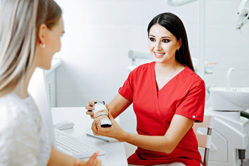 Obraz premium Concentrated dentist sitting at table and shows jaw samples tooth model to the patient