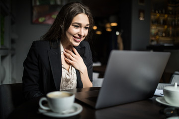 Portrait of a young beautiful businesswomen enjoying coffee during work on portable laptop.