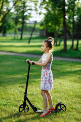 Cute little girl in rose dress drive the scooter on the meadow on sunset. Childhood concept.