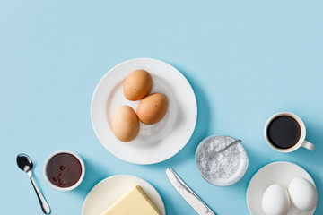 top view of fresh boiled eggs, butter, jam on white plates, yogurt with chia seeds, coffee, spoon...