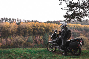 Rider standing with adventure motorcycle, Motorcyclist gear, A motorbike driver looks, concept of active lifestyle, enduro travel road trip. Evening, autumn. Tourist traveler. copy space