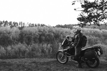 Obraz na płótnie Canvas Rider standing with adventure motorcycle, Motorcyclist gear, A motorbike driver, concept of active lifestyle, enduro travel road trip. Evening, autumn. Tourist traveler. copy space, black and white