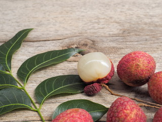 Fototapeta na wymiar a group delicious red ripe Lychees fruit with green leaves on wood texture background.