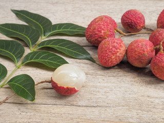 Obraz na płótnie Canvas a group delicious red ripe Lychees fruit with green leaves on wood texture background.