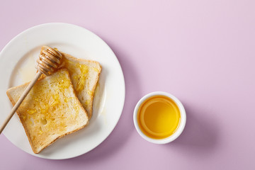 top view of bowl, toasts with honey on white plate and wooden dipper on violet background