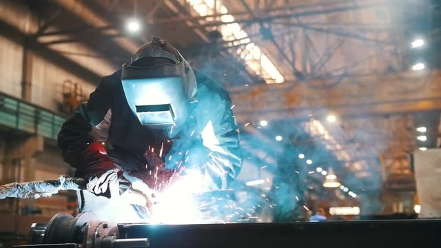 Construction plant. A man in a helmet using a welding machine to connect details