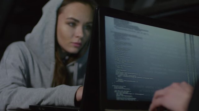 Rack focused shot of two female programmers sitting at table in darkness and programming together