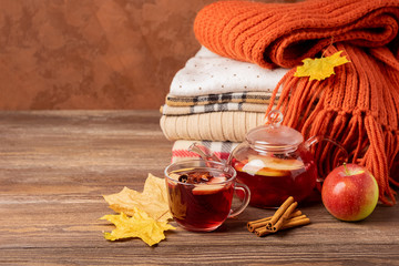 Drink autumn apple red berries in a glass cup and kettle and a stack of knitted clothes on a wooden...