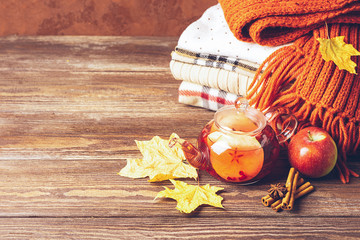 Drink autumn apple red berries in a glass cup and kettle and a stack of knitted clothes on a wooden...