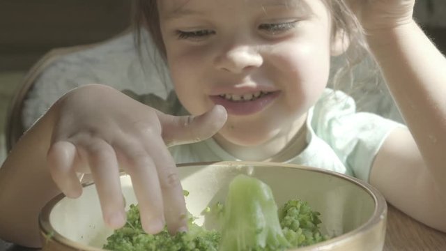Happy little girl hate eating broccoli vegetables on a plate with hands