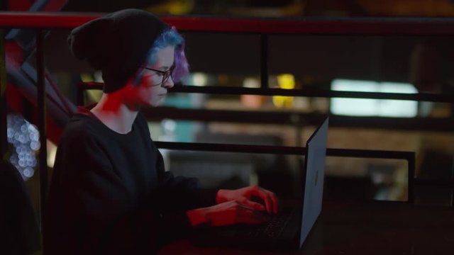 Lockdown of young woman-hipster sitting at caf&eacute; table at laptop and typing on keyboard