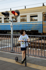 A little boy rides a scooter near the railroad crossing while train is coming.