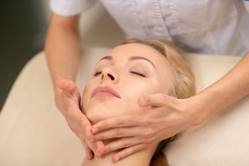 Fototapeta na wymiar Blonde woman enjoying face massage in beauty salon