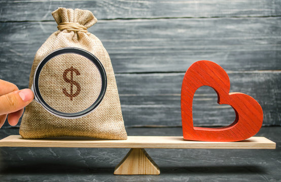 Bag With Money And Red Wooden Heart On The Scales. Money Versus Love Concept. Passion Versus Profit. Family Or Career Choice. Family Psychology. Mind Vs. Passion