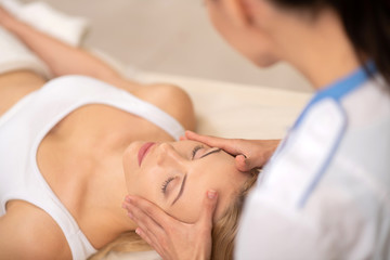 Obraz na płótnie Canvas Woman wearing white top enjoying face massage in salon
