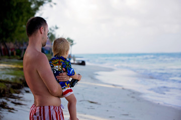 Dad, holding little toddler boy with binoculars, observing dolphins