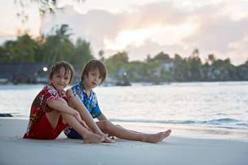 Obraz premium Happy beautiful fashion family, children, dressed in hawaiian shirts, playing together on the beach on sunset