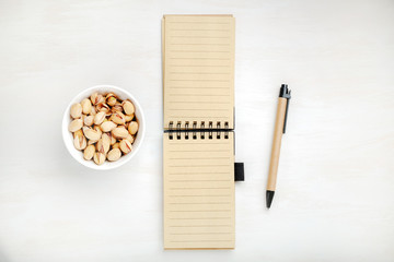 Notebook with pen, and a bowl of pistachios. The concept of planning