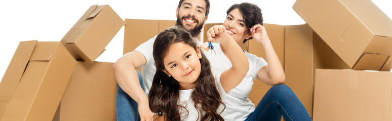 panoramic shot of of happy latin kid holding keys near parents and boxes isolated on white