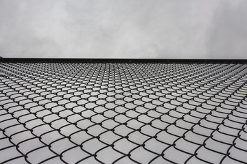Looking Looking up at the protective metal fence and iron mesh outside the city sports fieldup at...