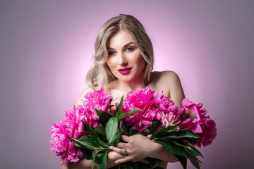 Close up portrait of an attractive young woman holding flowers pions bouquet on pink background