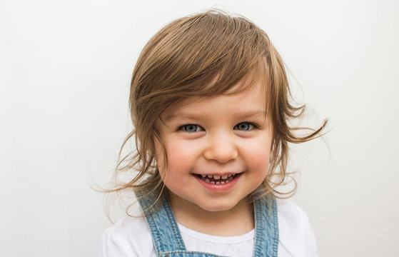 Happy beautiful Caucasian toddler with blue eyes smiling laughing portrait on neutral background