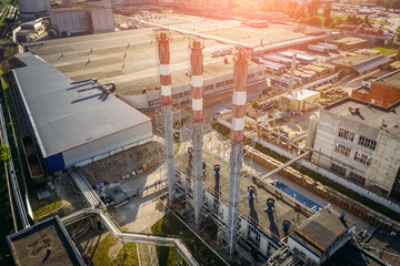Aerial view of industrial area with warehouses, factory buildings and chimney on foreground at sunset, drone photo