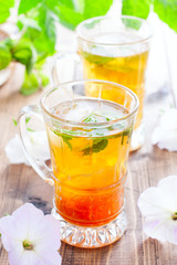 Black iced tea with lemon and mint in glass cups on a wooden table, selective focus
