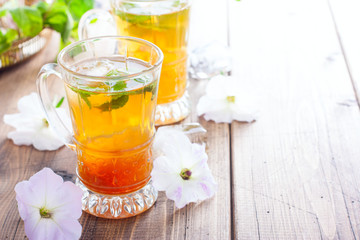 Black iced tea with lemon and mint in glass cups on a wooden table, horizontal, copy space