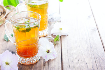 Black iced tea with lemon and mint in glass cups on a wooden table, horizontal, copy space