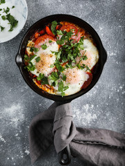 Traditional Israeli Cuisine dishes Shakshuka. In a Cast Iron Pan. Middle eastern style eggs poached in tomato and pepper sauce with parsley, onion and spices on grey concrete background. Top view.