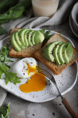 Toasts with avocado, arugula and poached egg on handmade plate. Copyspace.