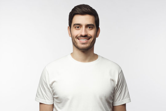 Portrait of smiling handsome man in white t-shirt looking at camera, isolated on gray background