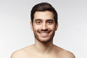 Naklejka premium Skin care. Close-up portrait of handsome smiling shirtless man with bristle, looking at camera, isolated on gray background