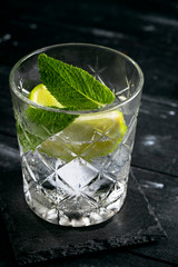 Gin and Tonic cocktail with lime, mint and ice, alcoholic drink in a glass on a dark wooden background, close up