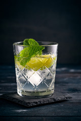 Gin and Tonic cocktail with lime, mint and ice, alcoholic drink in a glass on a dark wooden background, copy space