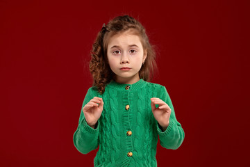 Portrait of a little brunette girl with a long, curly hair posing against a red background.