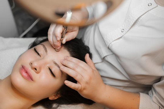 Upper view of a lovely caucasian woman doing microdermabrasion procedure on her face in spa wellness center.