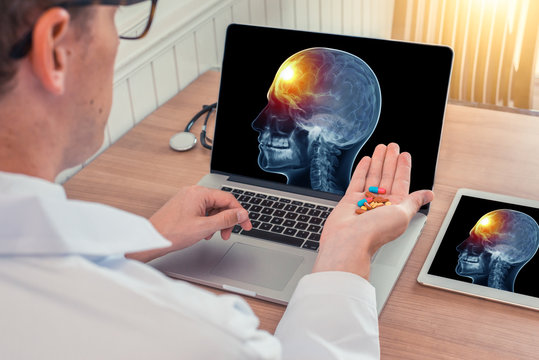 Doctor holding pills with x-ray of skull head with pain in the front of the brain on a laptop. Digital tablet on the wooden desk