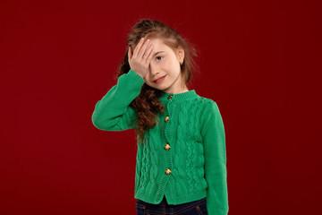 Portrait of a little brunette girl with a long, curly hair posing against a red background.