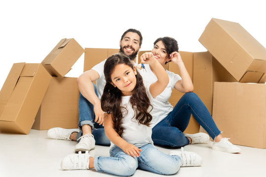 selective focus of happy latin kid holding keys and sitting near parents and boxes isolated on white