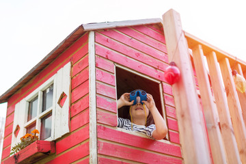 Boy in a wooden playhouse looking through a binocular