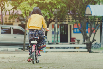 Back view of female teacher rides bicycle to teach students at classroom.