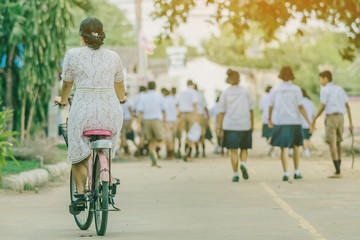 Back view of female teacher rides bicycle to teach students at classroom.