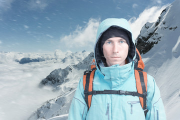 Fototapeta na wymiar Young male mountain climber on winter mountain top view looking at camera. Front view. Active lifestyle in cold weather. Winter mountain landscape and cloudy sky. Active lifestyle and tourism.