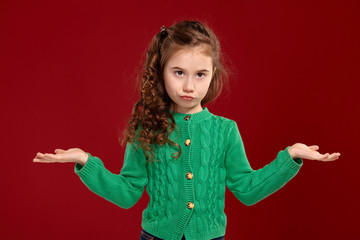 Portrait of a little brunette girl with a long, curly hair posing against a red background.