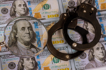 100 US dollars banknotes under magnifying glass of counterfeit money and handcuffs