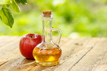 Apple vinegar in glass bottle and fresh red apple on wooden boar