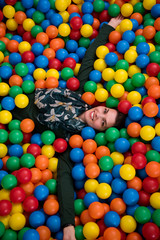 Fototapeta na wymiar young mom playing with kids in pool with colorful balls