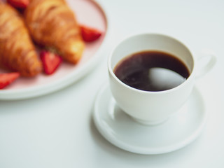 Summer breakfast focused on the cup of coffee and plate with croissants on background